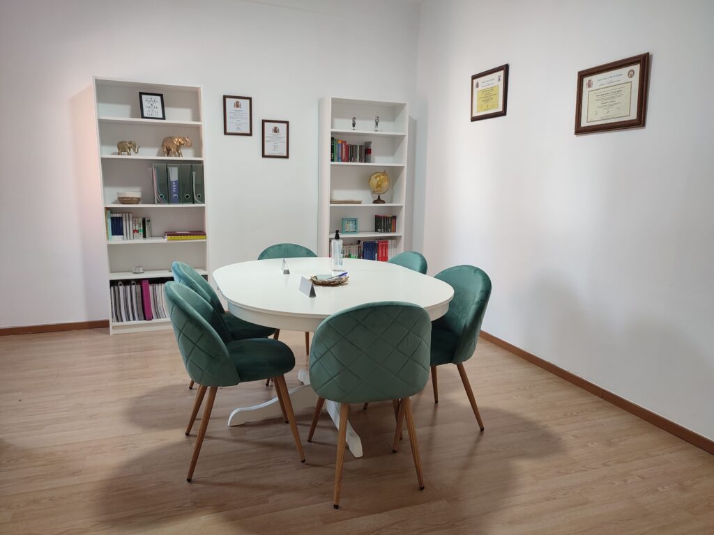 Sala de reuniones de Lemnis Abogadas con sillas de terciopelo verde y una mesa redonda, evocando un ambiente de apoyo y disponibilidad constante para los clientes, tal como sugiere el lema 'Siempre a tu lado'.
